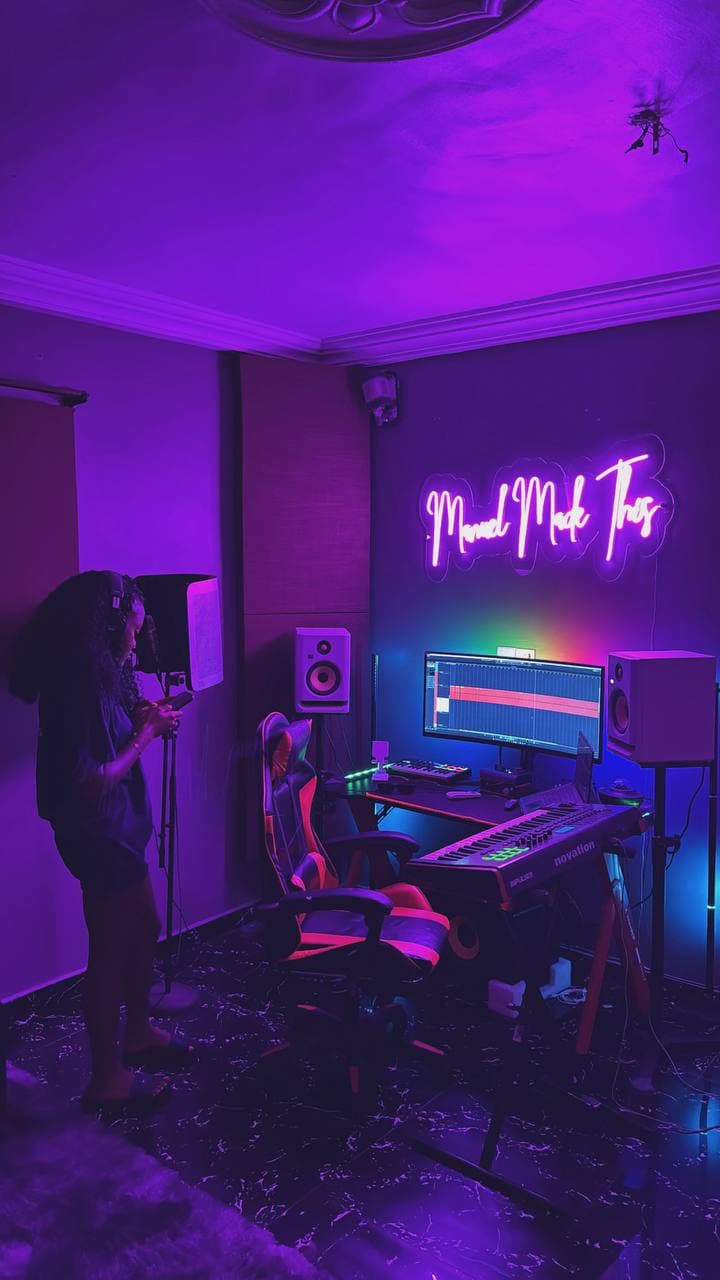 An artist at the vocal booth microphone, with the desk and neon sign behind