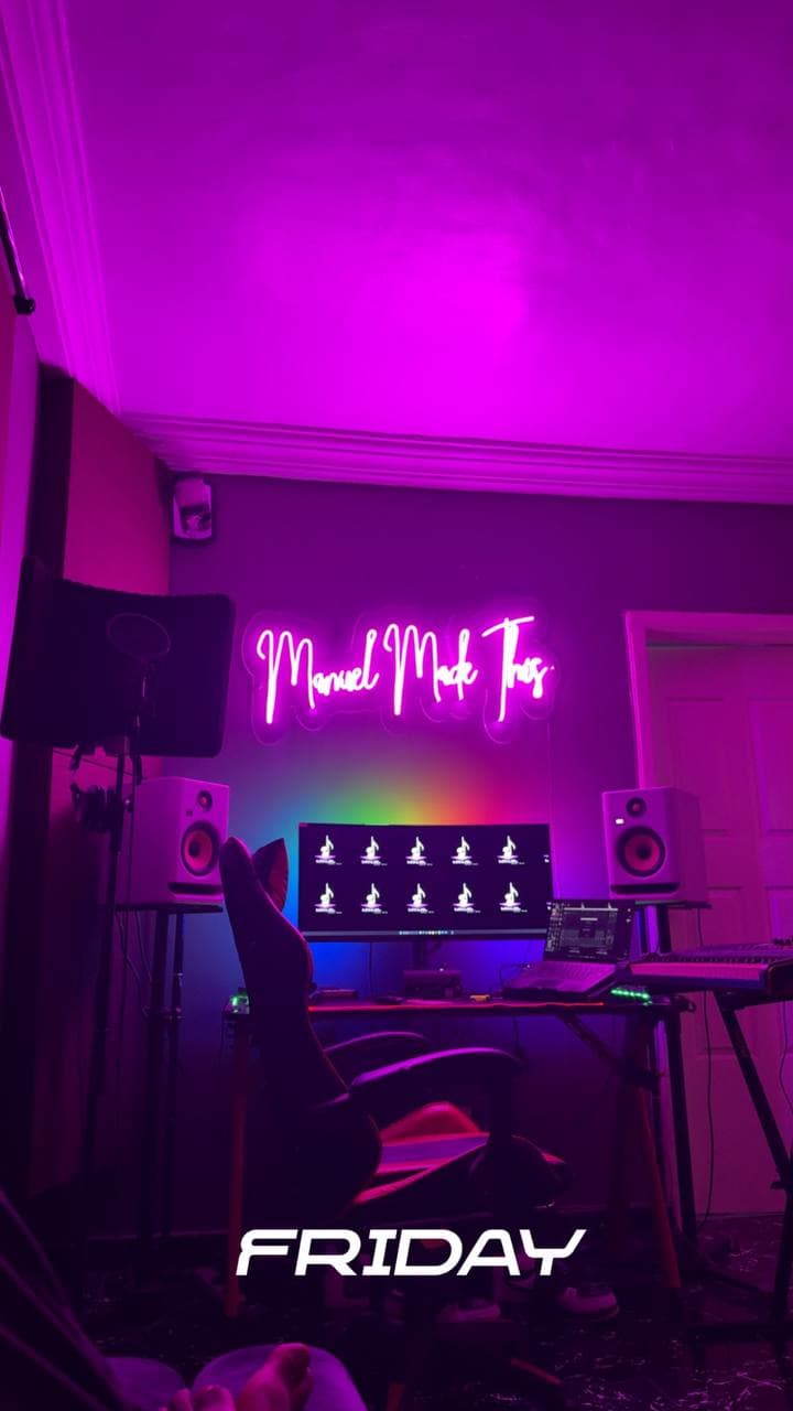 The studio desk under pink light below the ManuelMadeThis neon sign, with “Friday” written across the photo