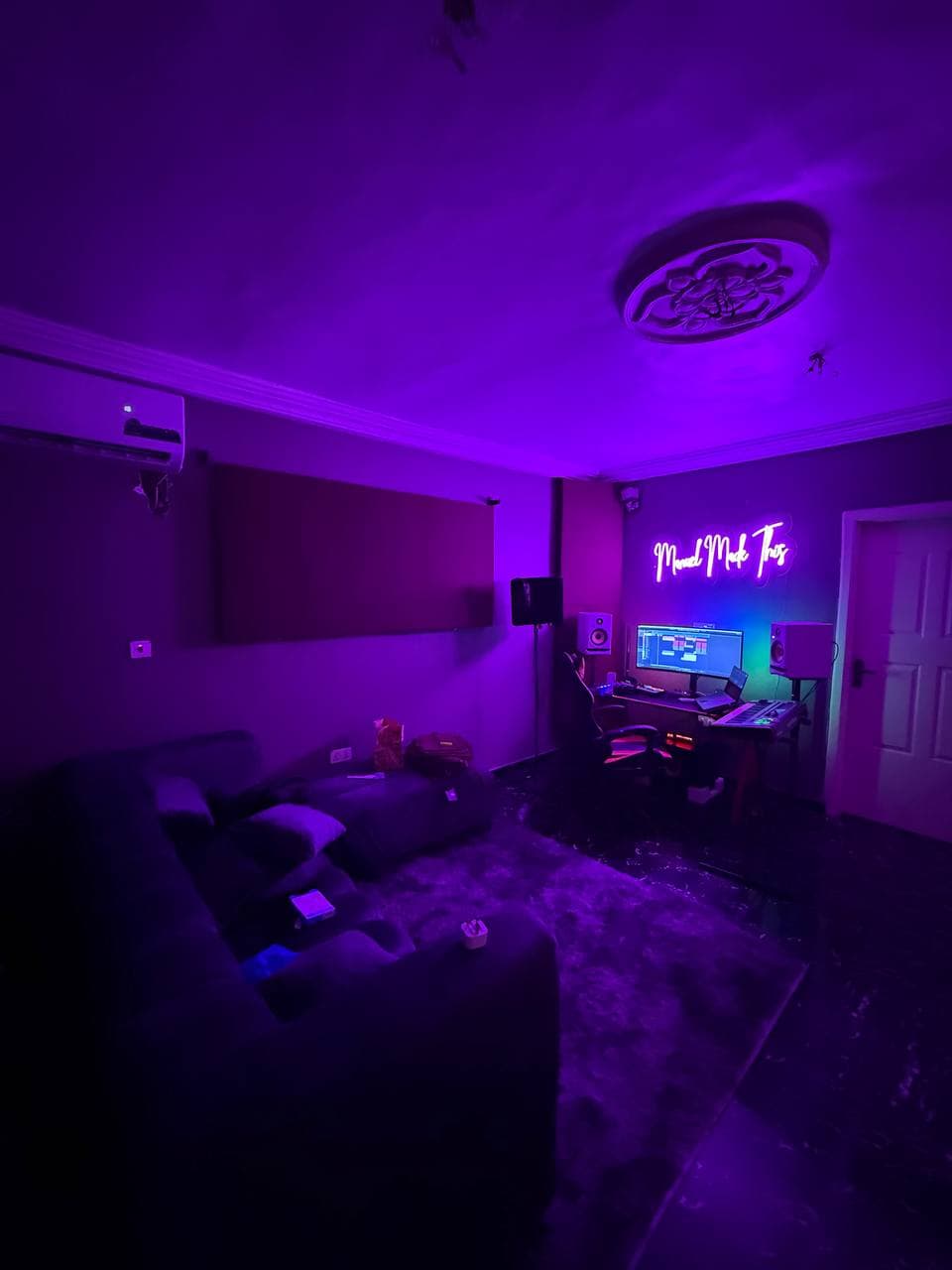 A wide view of the studio: a sofa and rug in front, the desk and neon sign at the far wall